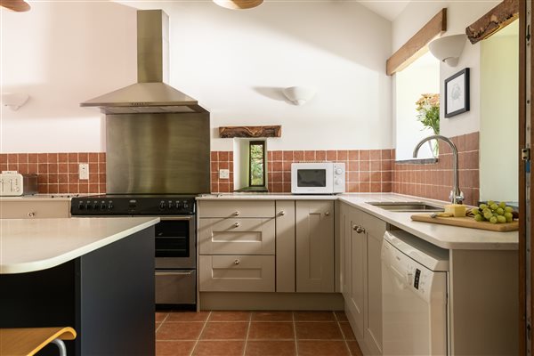 Kitchen cupboards, tiled floor and splash backs, range cooker with hood above.